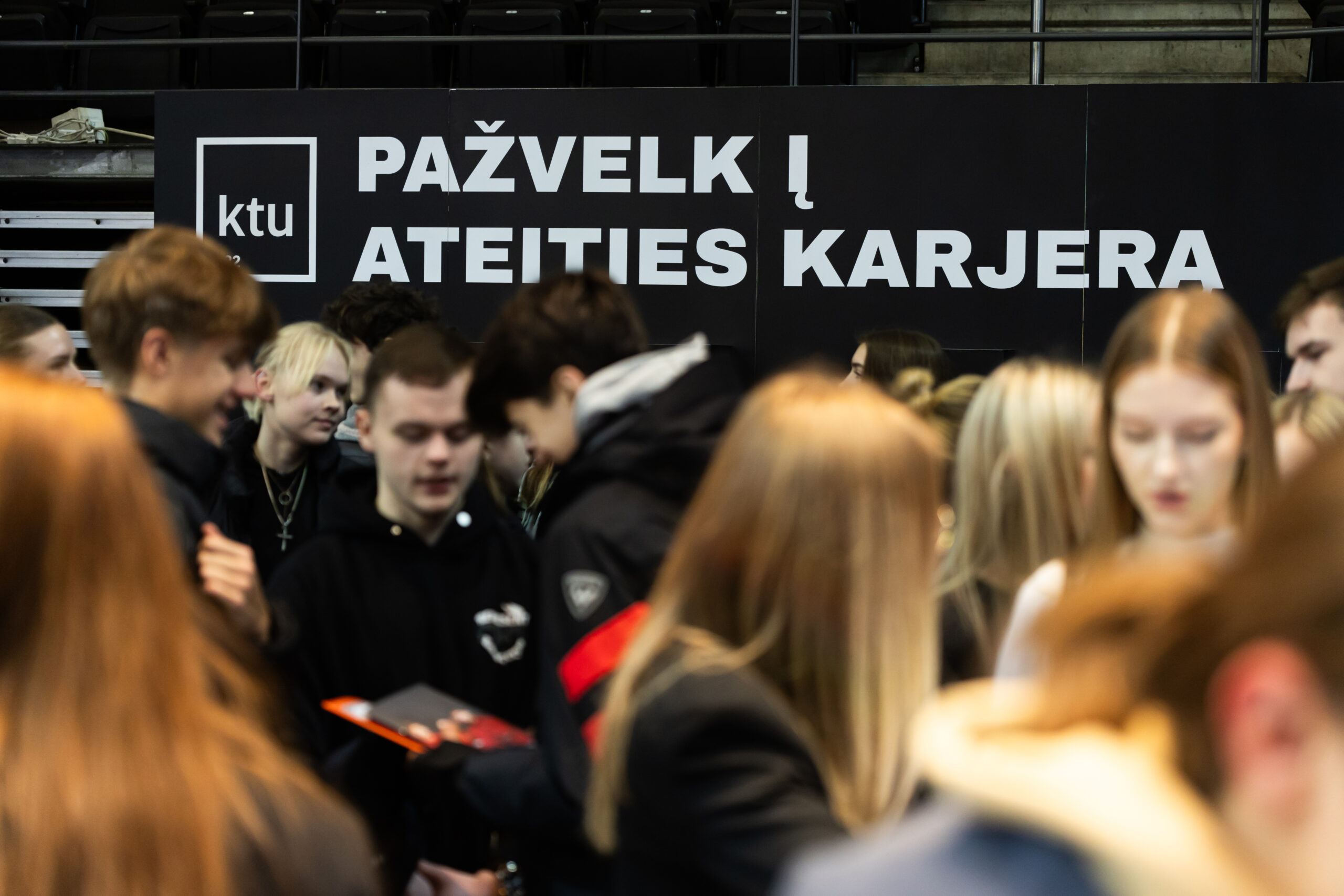 Minia jaunuolių konsultuojasi apie studijų pasirinkimą. Fone didelis KTU stendas su užra&scaron;u - Pažvelk į ateities karjerą.